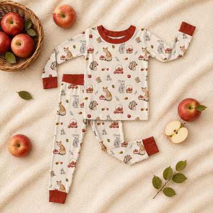 Children's bamboo pajama set with woodland animals and autumn-themed design on a beige blanket with apples and leaves.
