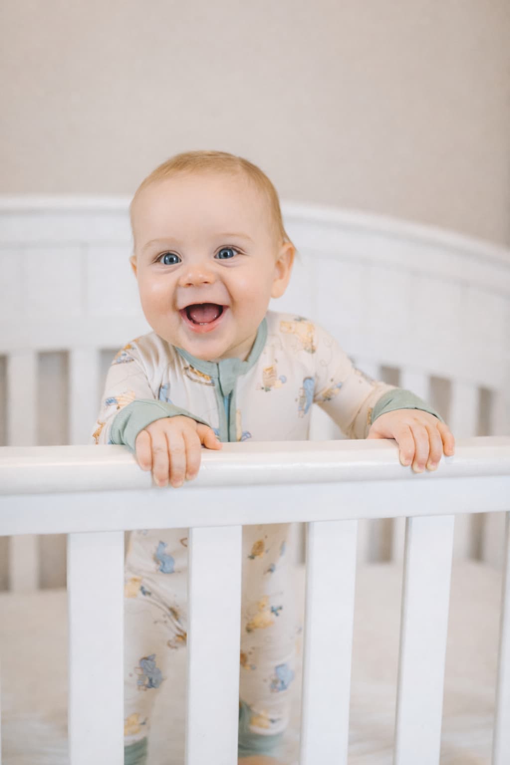 Baby standing in a crib wearing a Classic Pooh patterned bamboo sleeper pajamas with a neutral background.