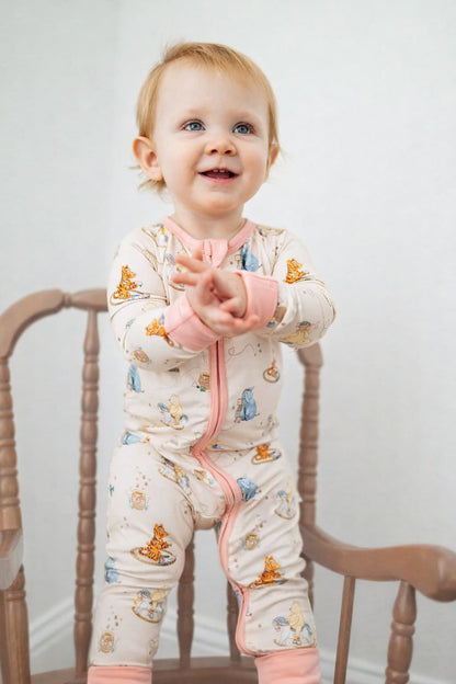 Child wearing a Classic Pooh bamboo sleeper pajamas with pink accents, standing on a wooden chair against a plain background.