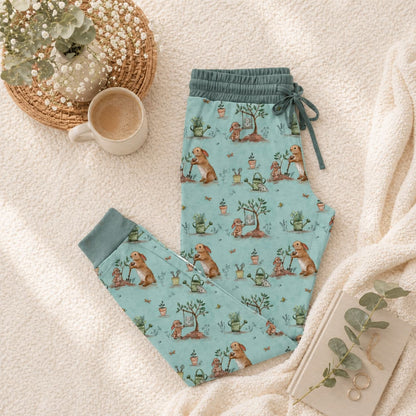 Light blue adult bamboo pajama pants with bunnies and plant pattern on a soft surface with a coffee cup and plant.