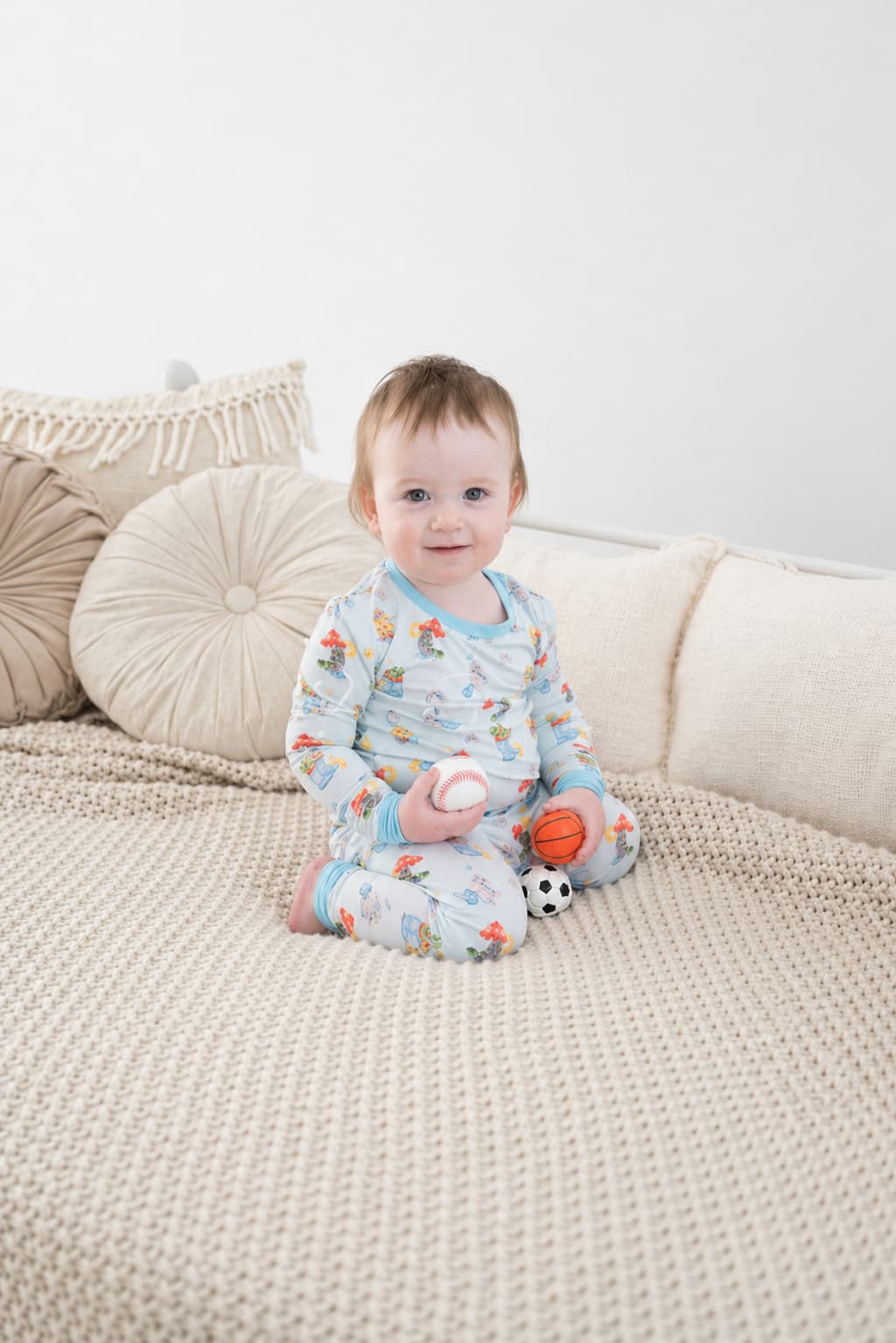 Child wearing light blue bamboo pajamas set with bunny pattern, sitting on a cream colored bed.
