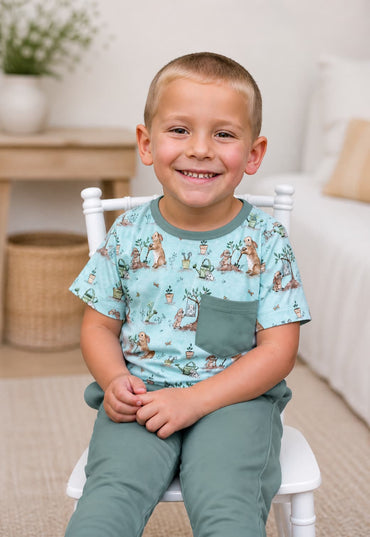 Child wearing a bunny patterned shirt with matching bamboo grayish sage pants sitting on a white chair.