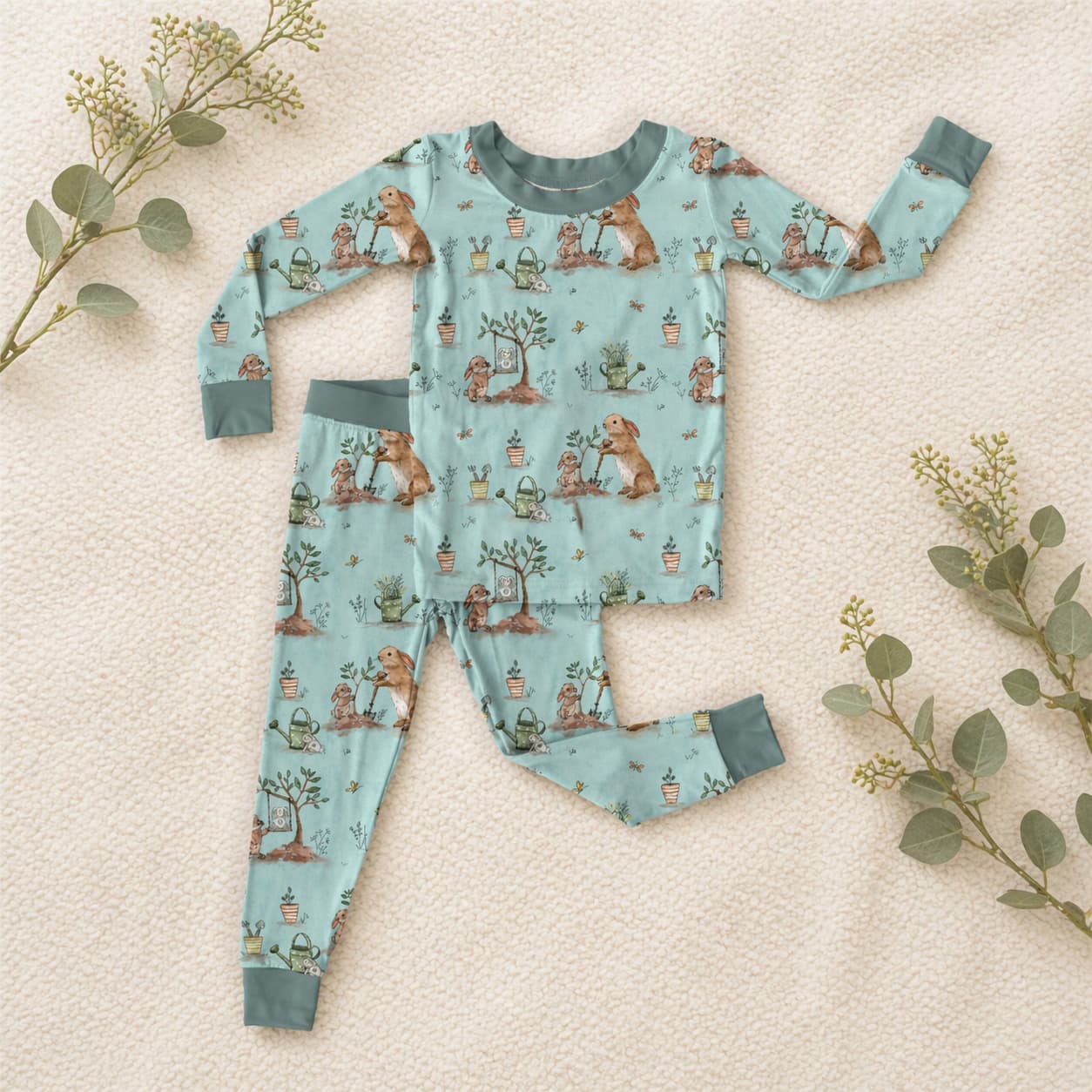 Children's bamboo viscose pajama set with bunny and gardening pattern on a soft beige surface with greenery.