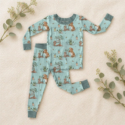 Children's bamboo viscose pajama set with bunny and gardening pattern on a soft beige surface with greenery.