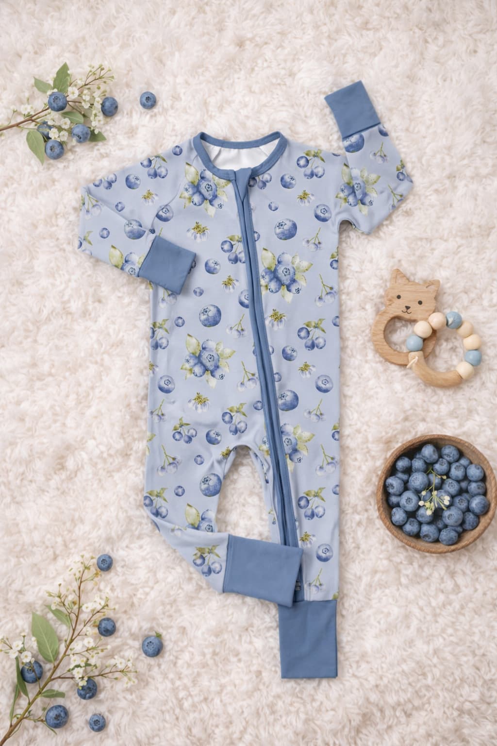 Bamboo pajamas sleeper in watercolor blueberry pattern on a textured surface with toys and blueberries.
