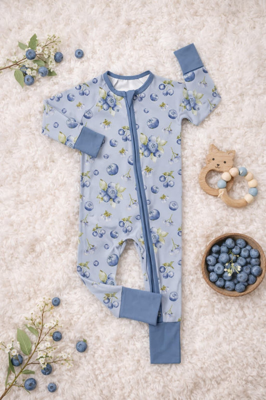 Bamboo pajamas sleeper in watercolor blueberry pattern on a textured surface with toys and blueberries.