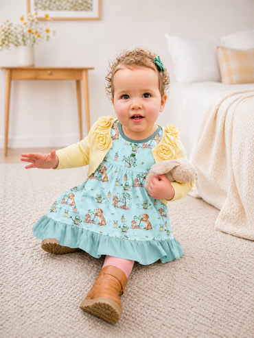 Girl wearing a blue bunny bamboo twirl dress with a light ywllow cardigan sitting in her bedroom.