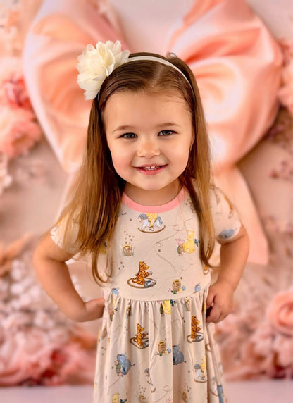 Young girl in a Winnie the Pooh bamboo twirl dress with a floral headband against a pink floral background