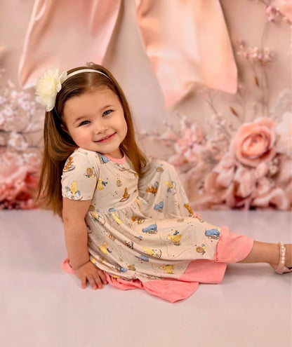 Young girl in a Classic Pooh bamboo twirl dress witting on a cream floor with a pink background