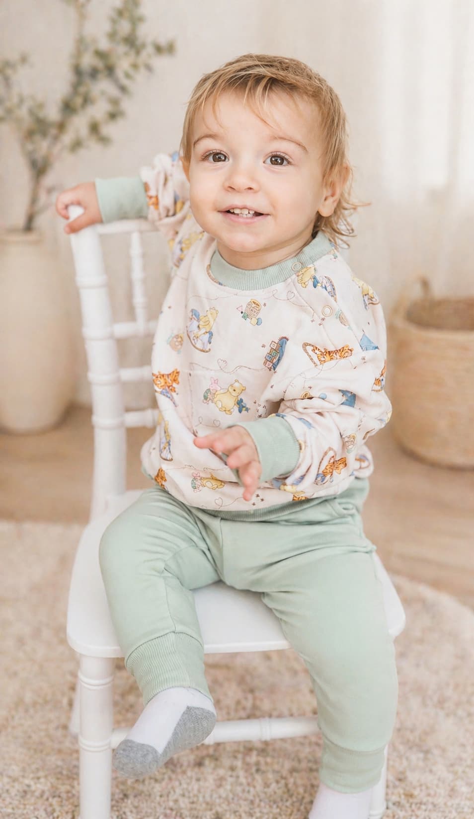 Child wearing a Classic Pooh bamboo french terry sweatshirt with light green pants sitting on a white chair.