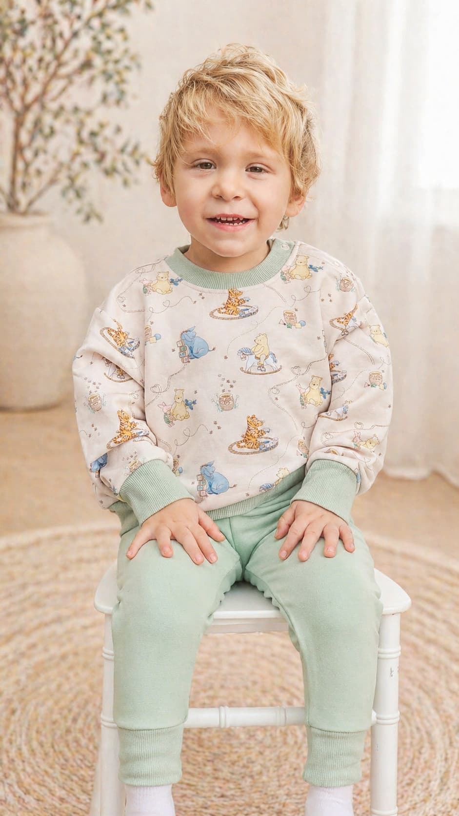 Child wearing a Classic Pooh bamboo french terry sweatshirt and green pants sitting on a chair.