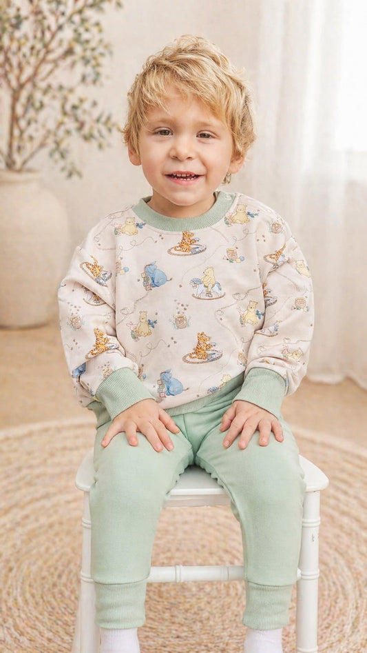 Child wearing a Classic Pooh bamboo french terry sweatshirt and green pants sitting on a chair.