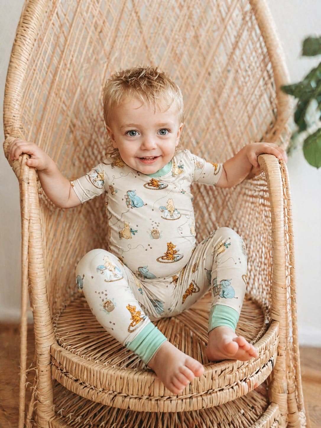 Child wearing a cream Classic Pooh bamboo pajamas set sitting on a wicker chair