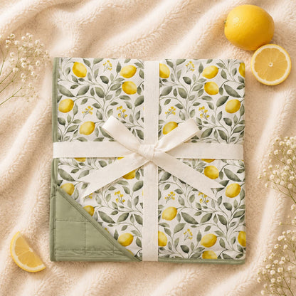 A folded bamboo quilted blanket with a trailing lemon pattern. Soft bamboo blanket oversized and wrapped in a cream ribbon, presented in a styled flat-lay.