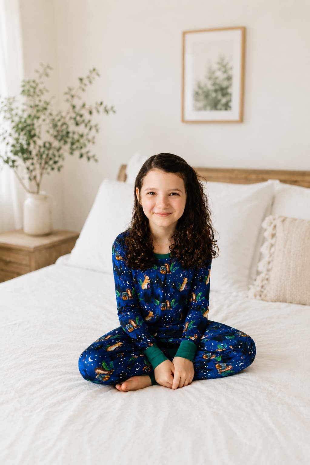 Girl wearing woodland bamboo pajamas sittting on a white bed. 
