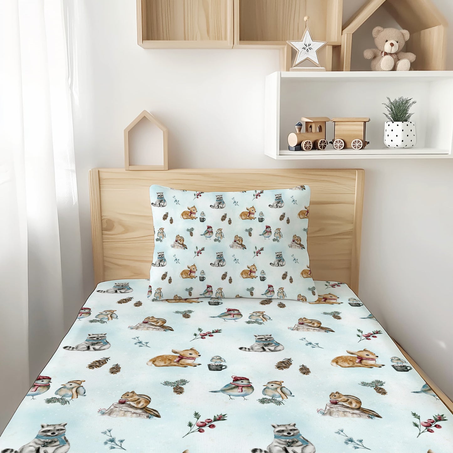 A light wood twin or full bed with a soft bamboo sheet and matching pillowcase printed with a colorful pattern of woodland animals, set in a bright child's bedroom with white shelves and toys.