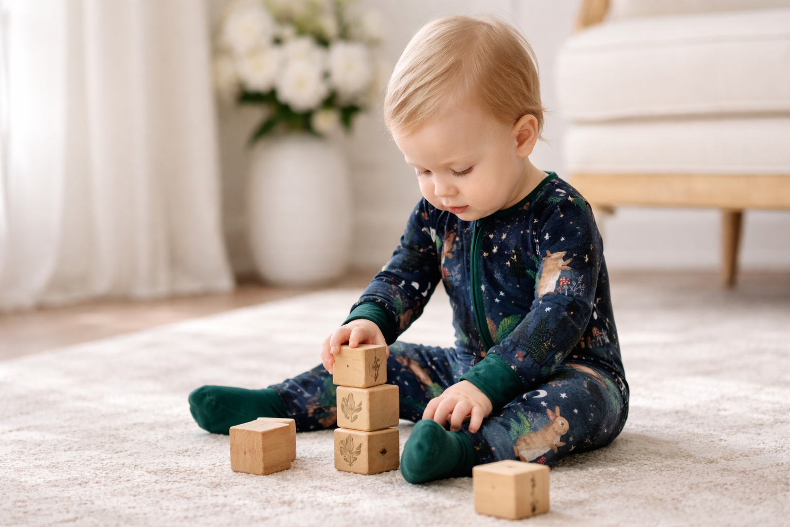 Baby in soft woodland bamboo sleeper playing with wooden blocks on a carpeted floor.