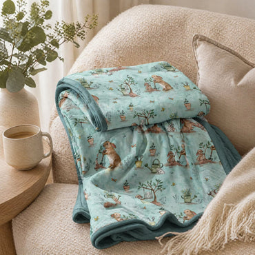 Folded bamboo blanket with bunnies and garden pattern on a couch next to a cup of coffee and plant.