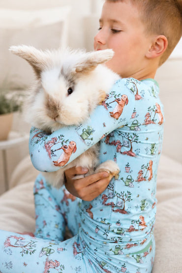 Boy hugging a white bunny while wearing a blue bamboo pajamas set with bunny print. 